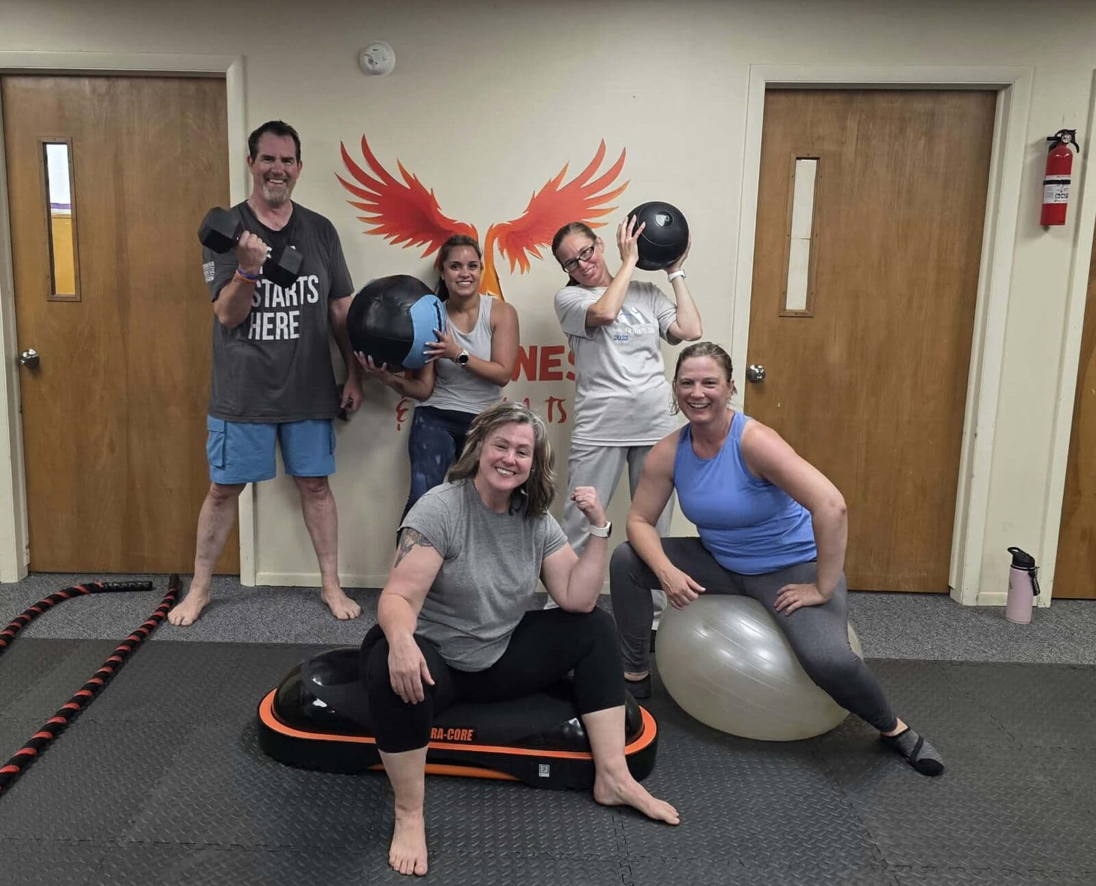 Members posing with kettlebells and medicine balls in front of the phoenix wall