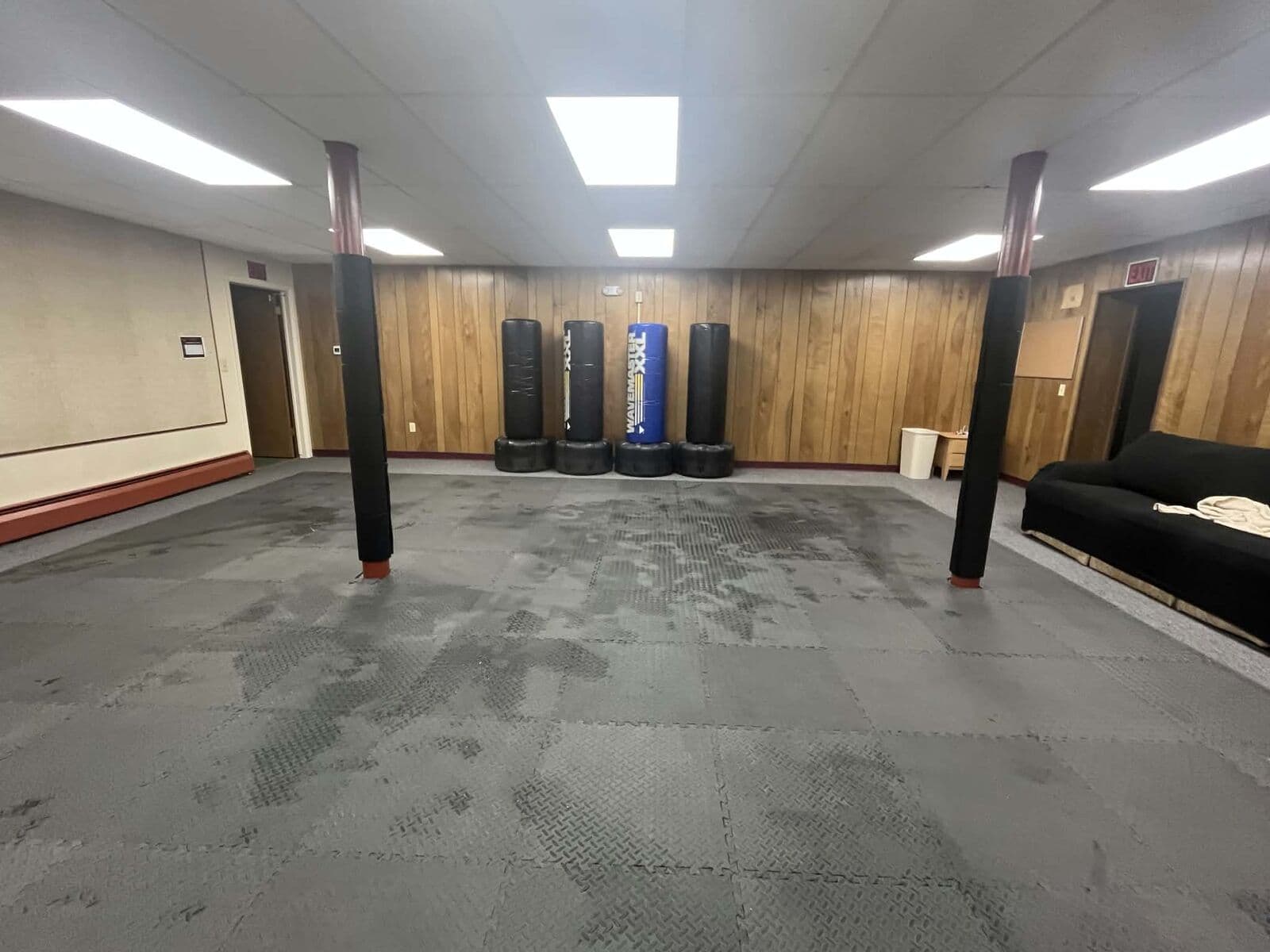 The matted basement training room with a row of heavy bags