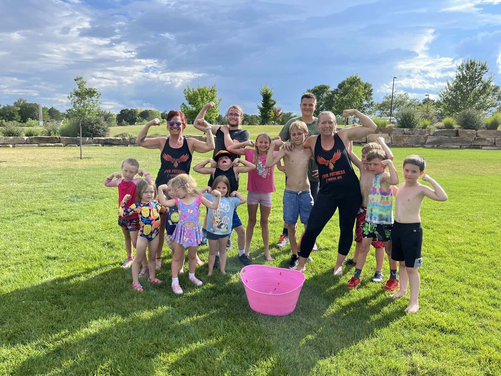 Kids and coaches flexing together on a grassy field